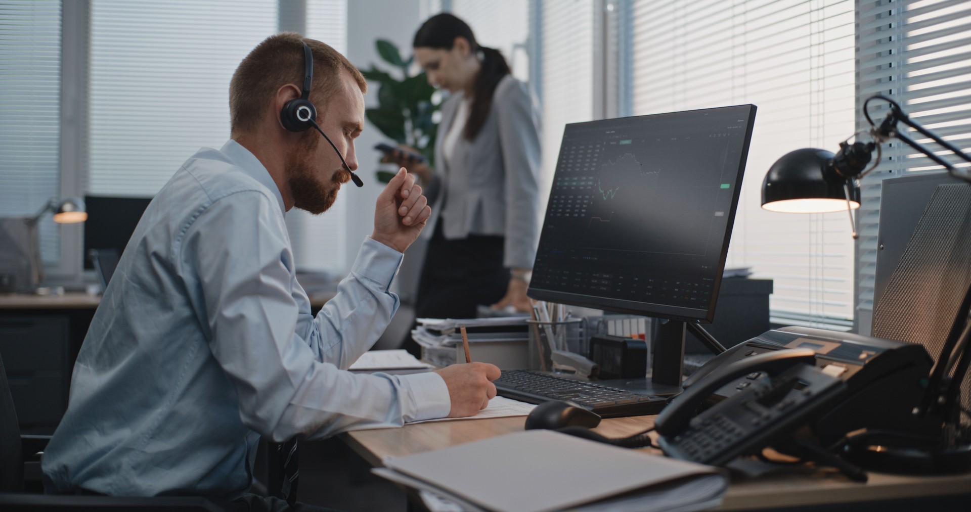 In modern office: Financial trader in headset works on computer, communicates with client